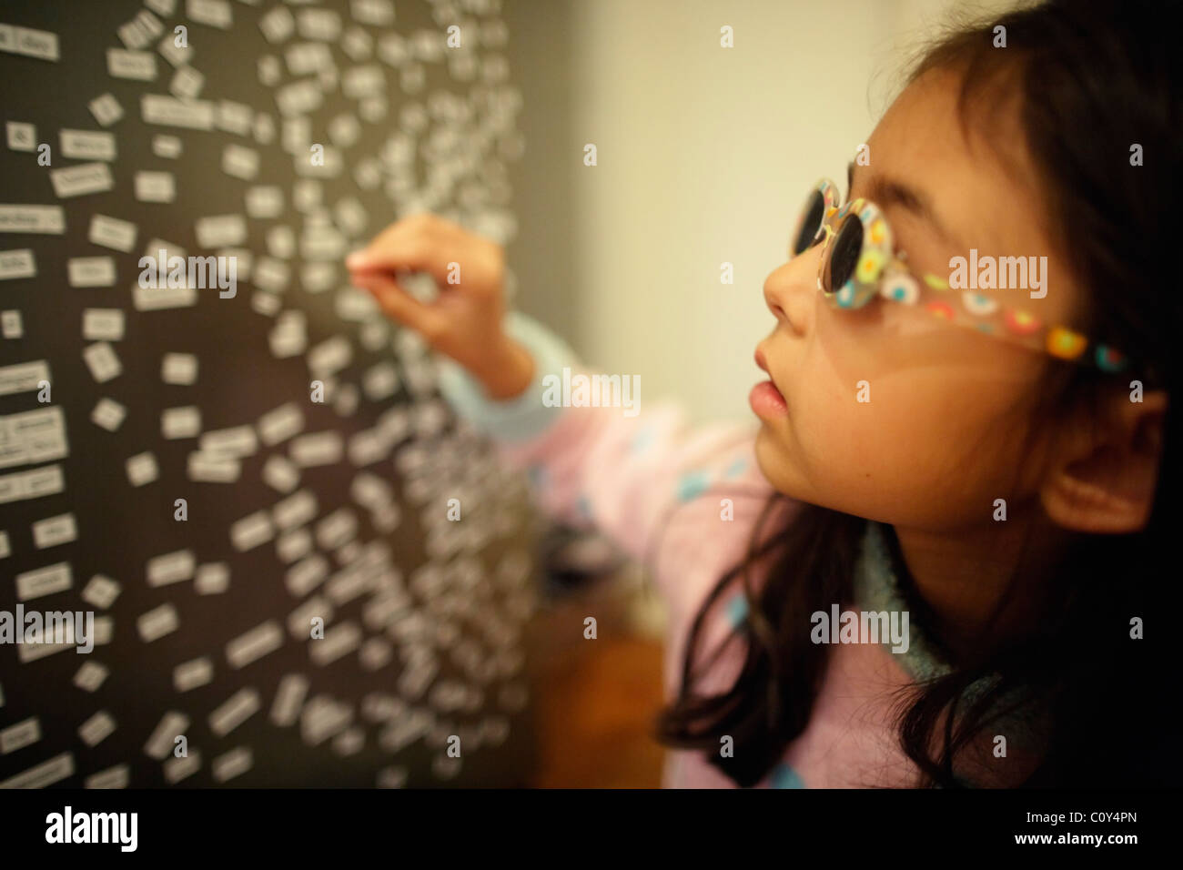 Girl wears sunglasses and plays with magnetic fridge words Stock Photo
