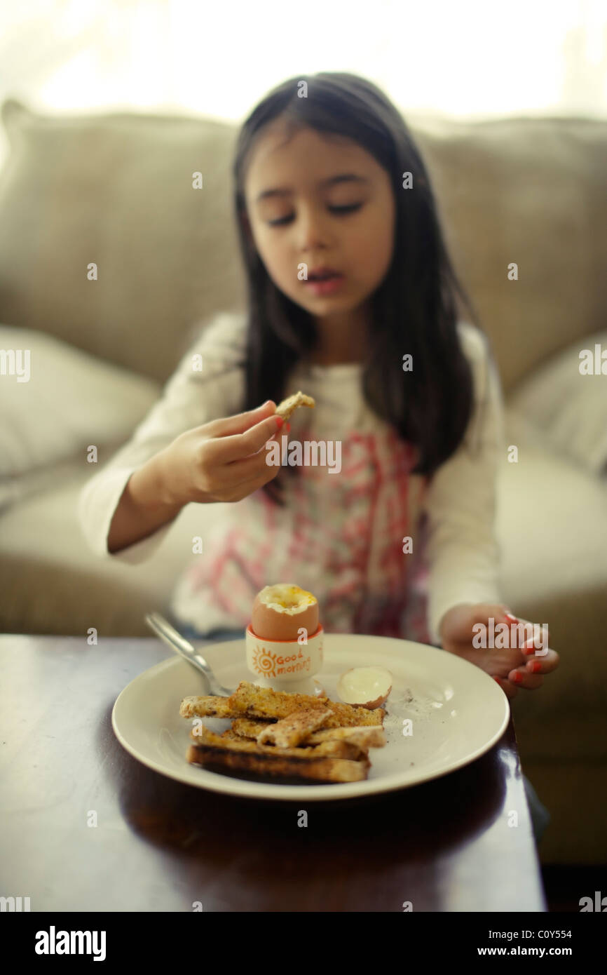 Girl eats boiled egg with toast soldiers for breakfast Stock Photo