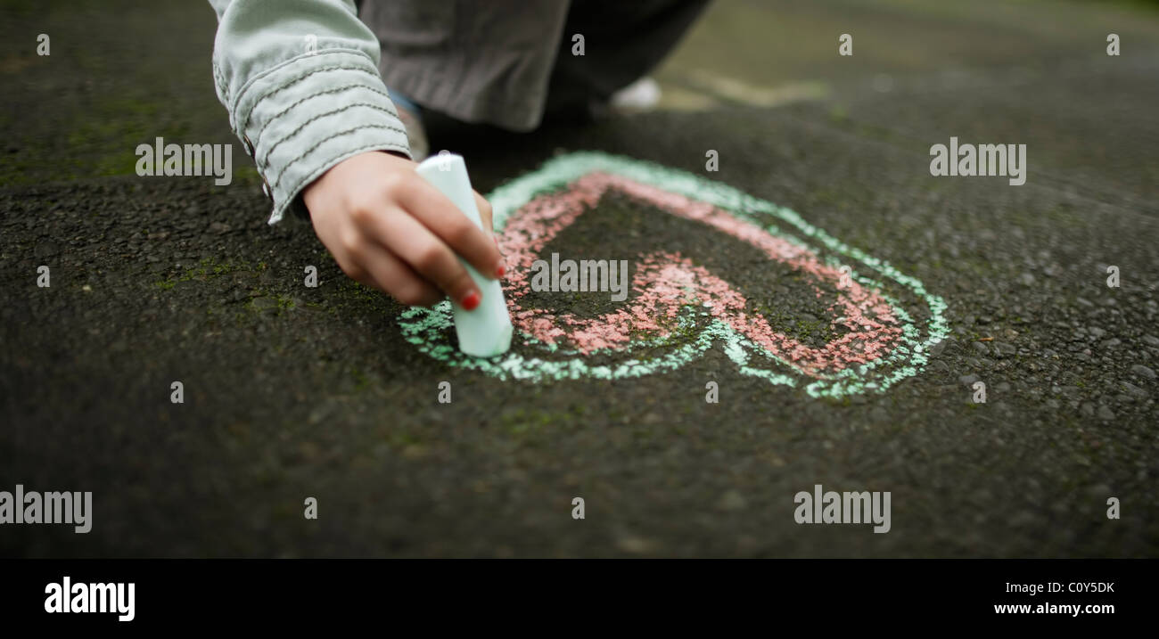 Girl drawing chalk heart on ground Stock Photo
