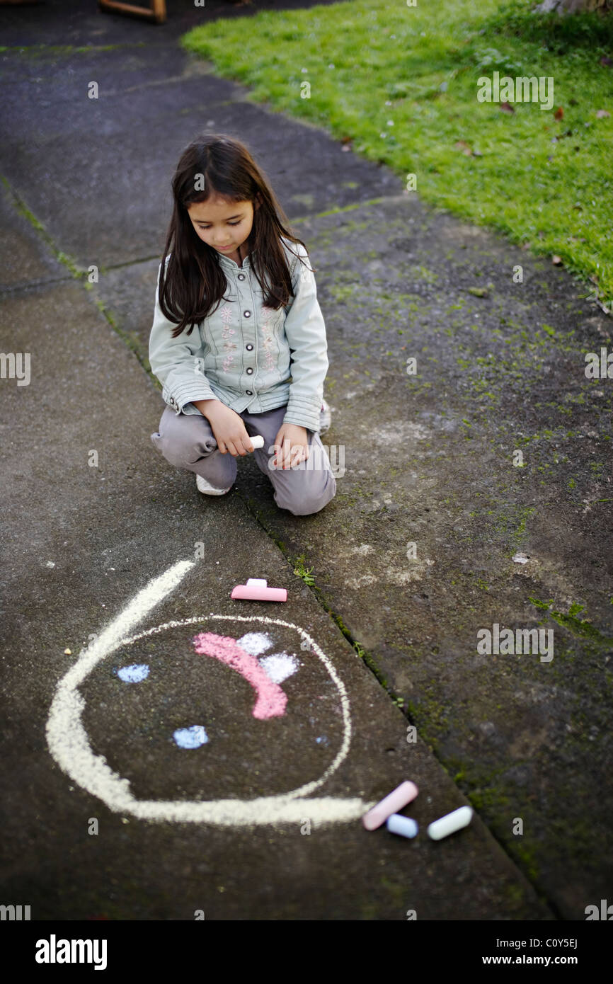 Girl draws face on path with chalk Stock Photo