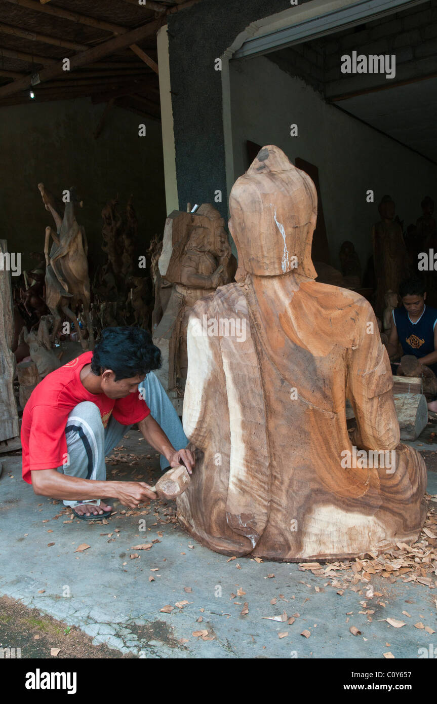 A Balinese craftsman wood carver at work on a carving of a large seated Buddha in the village of Peliatan Stock Photo