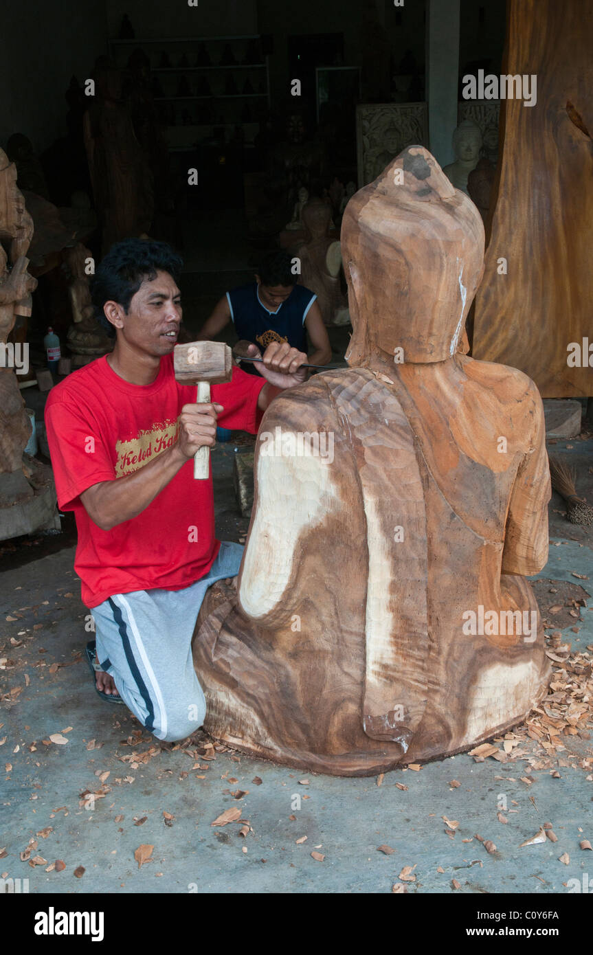 A Balinese craftsman wood carver at work on a carving of a large seated Buddha in the village of Peliatan Stock Photo