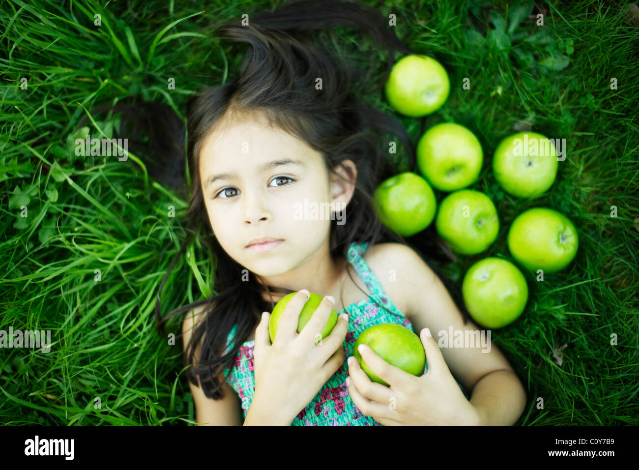 Six year old girl lies on grass with green apples Stock Photo