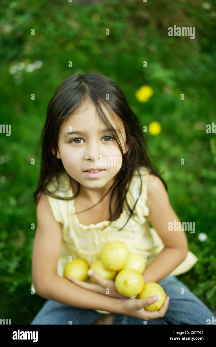 Six year old girl sits on lawn and holds lemons Stock Photo