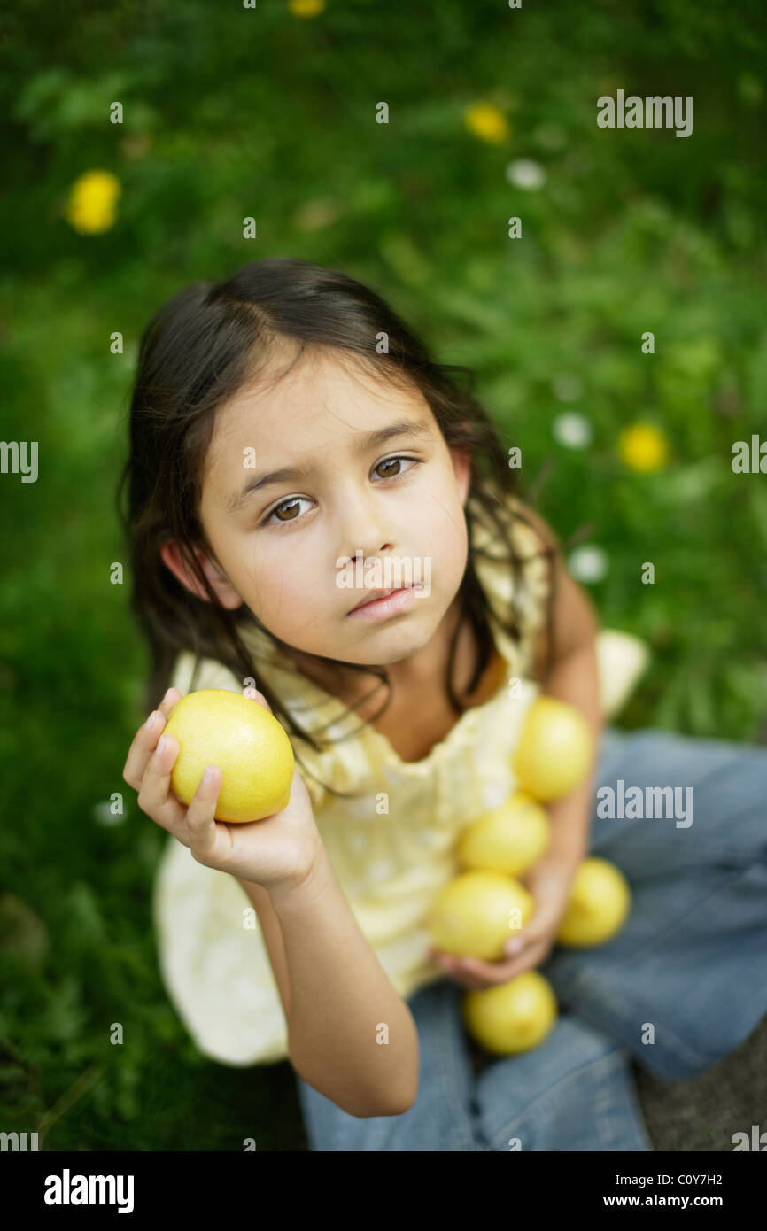 Six year old girl sits on lawn and holds lemons Stock Photo