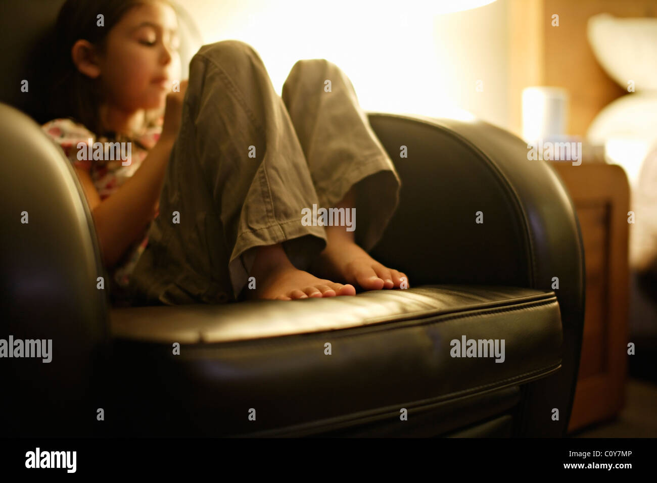 Girl draws up her feet and relaxes in armchair Stock Photo