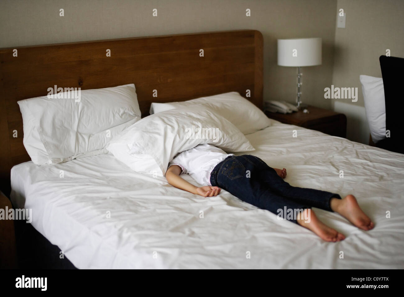 Girl lies on stomach on bed with head under pillow Stock Photo