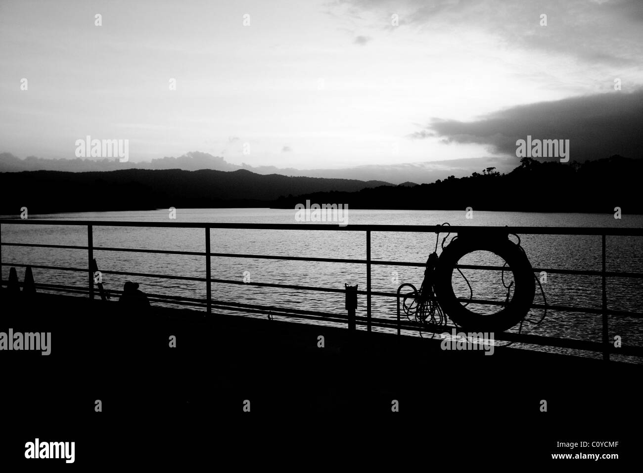 Life preserver on boat railing with nearby landmass. Silhouetted Stock Photo