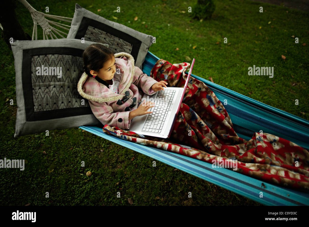 Girl sits in hammock with blanket using laptop computer on a cool evening. Stock Photo