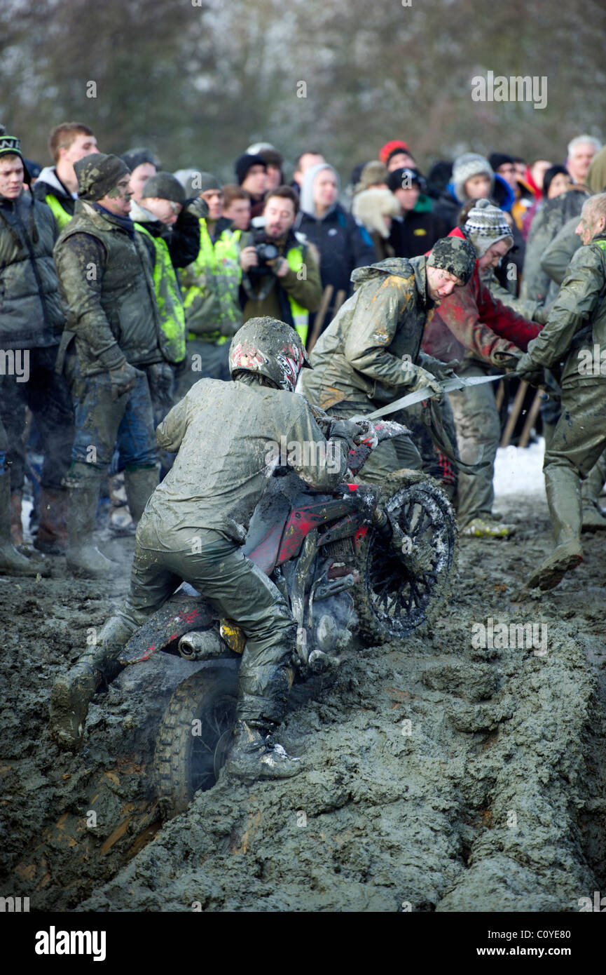 Man on muddy motocross scrambling motorcycle pulled by rope and team of helpers out of mud hole bog with steam rising Stock Photo