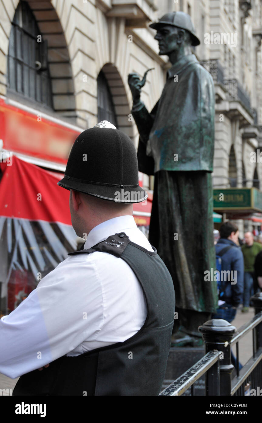 Beat policeman patrolling tourist area outside Baker Street Station with Sherlock Holmes sculpture beyond obscured sign Stock Photo