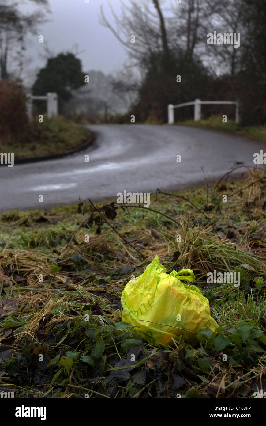 abandoned yellow plastic bag of rubbish on country grass verge Stock Photo