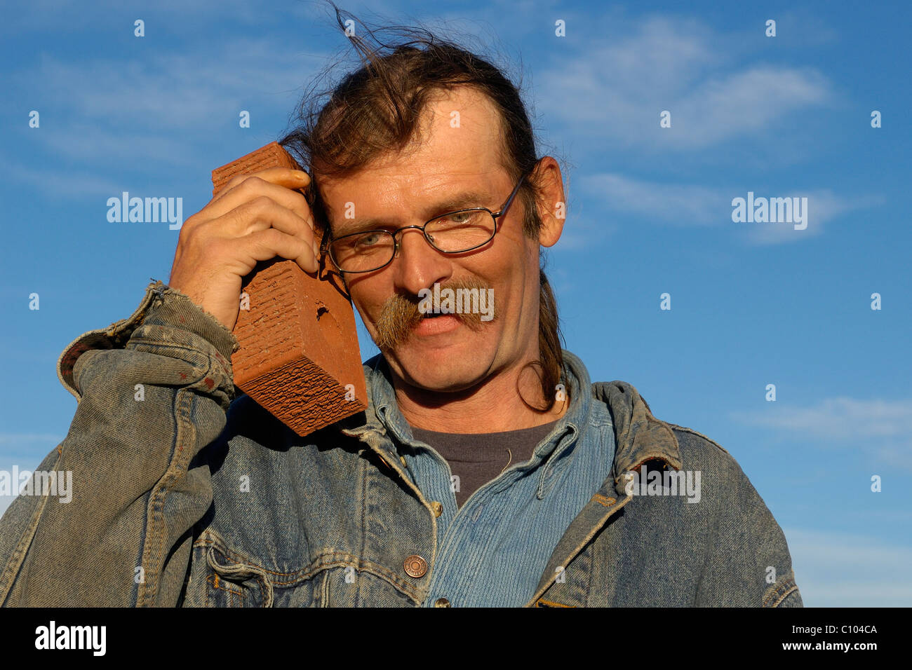 A scruffy man uses a brick as a cell phone Stock Photo