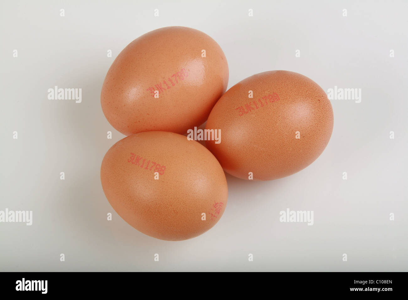 three brown eggs on a white background with sell by dates Stock Photo
