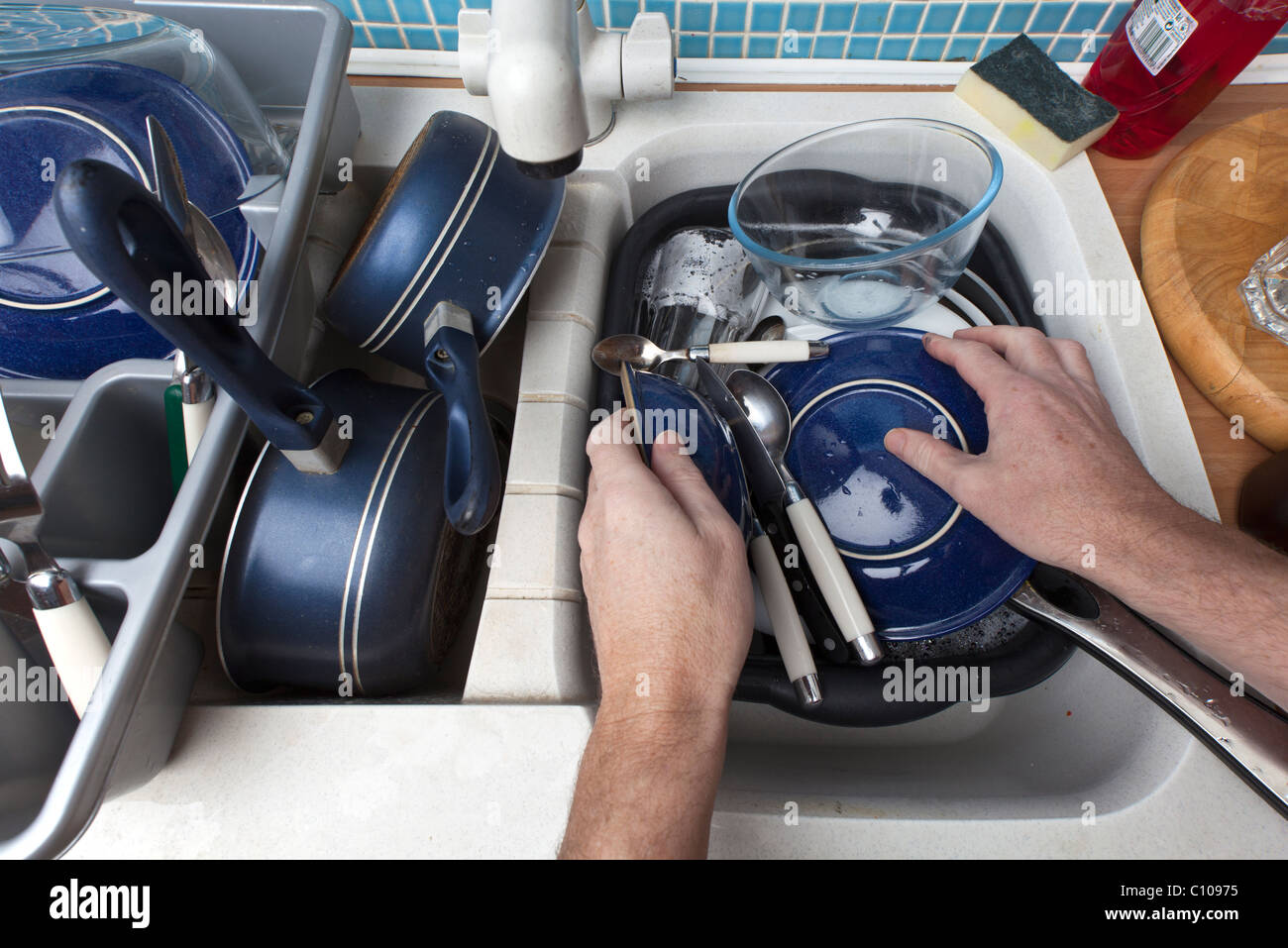 a pair of hands washing up a sink full of dirty dishes Stock Photo