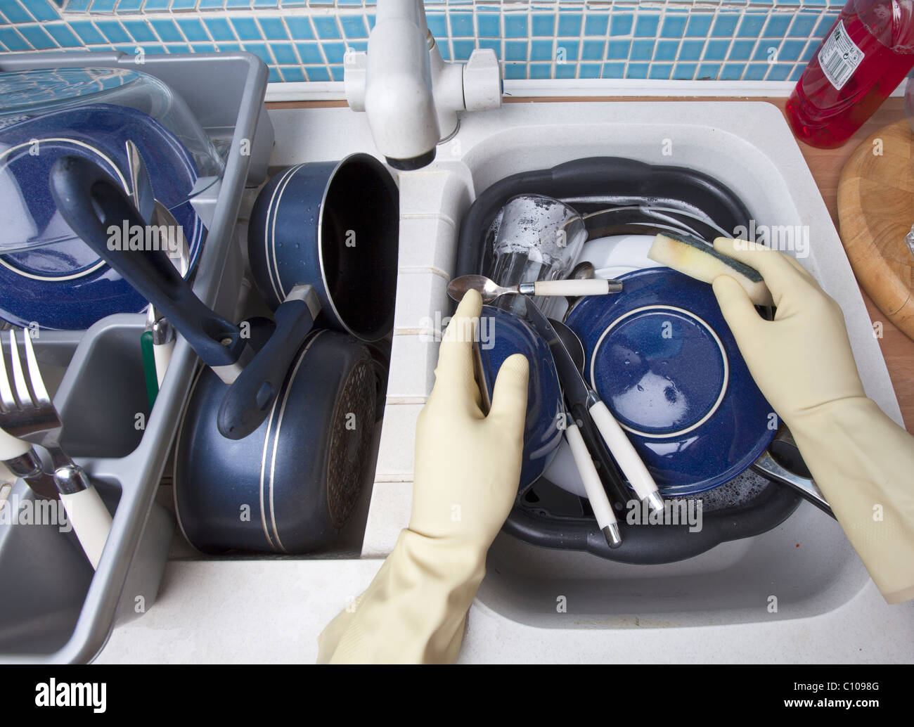 a pair of hands in yellow rubber gloves washing dishes in a kitchen ...