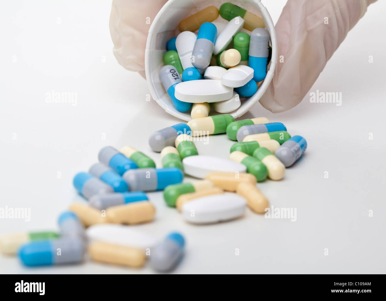 a plastic gloved hand dispensing a variety of prescription medicine from a paper dispensing cup Stock Photo