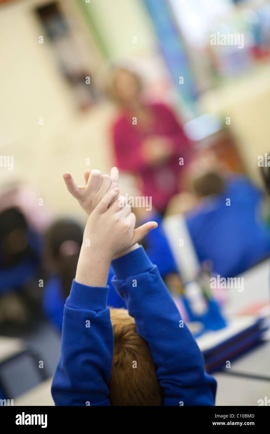 Group of school kids in classroom with hands up wanting to answer