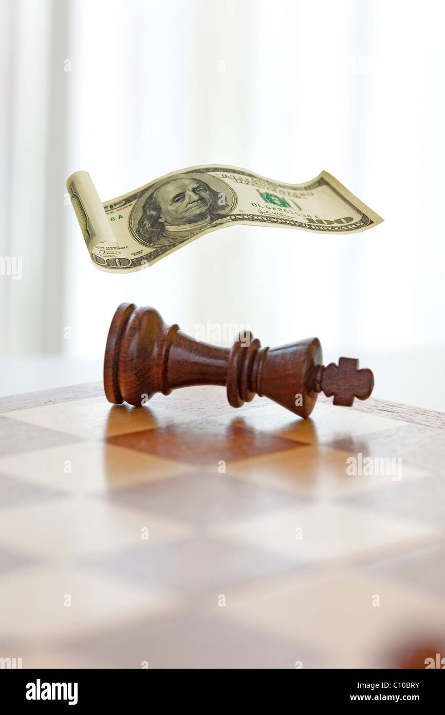chess game king knocked over covered with a floating one hundred dollar bill. Stock Photo