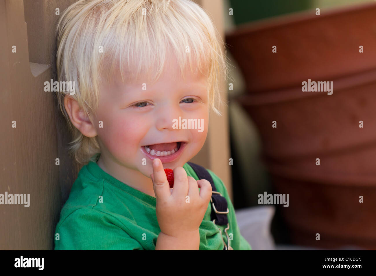 A boy hiding from the sun on a warm, bright summers day, eating a strawberry. Stock Photo