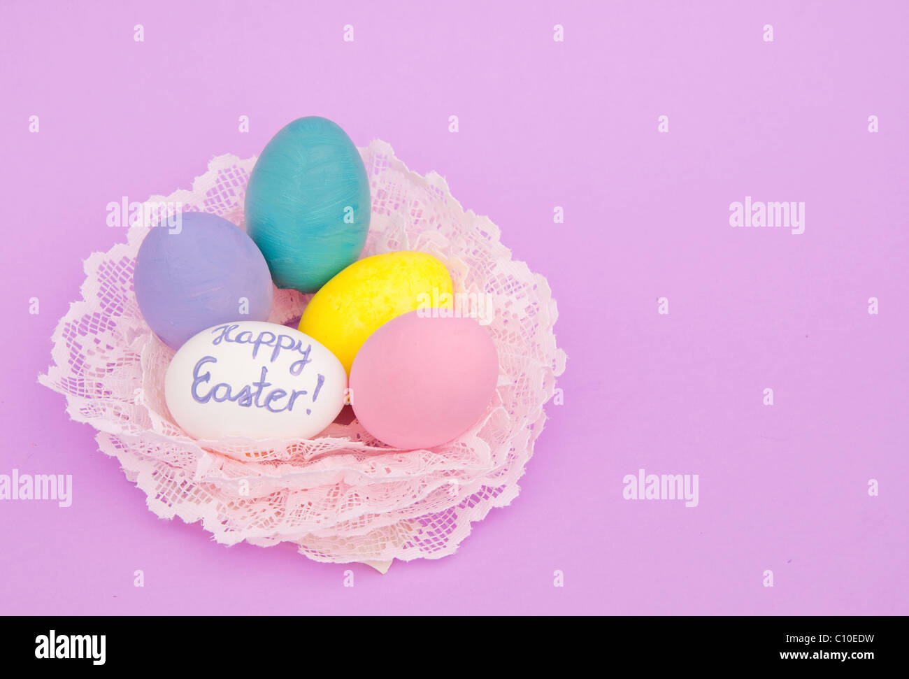 Hand painted pastel colored Easter eggs in a nest made of pink lace, on light purple background, with copy space Stock Photo