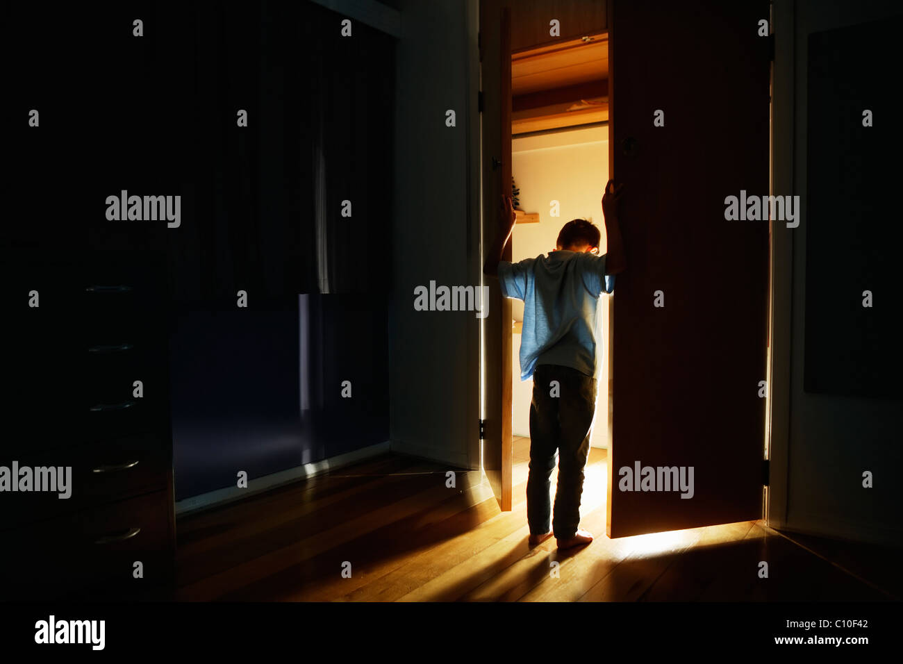 Boy stands at cupboard doors lit from within Stock Photo