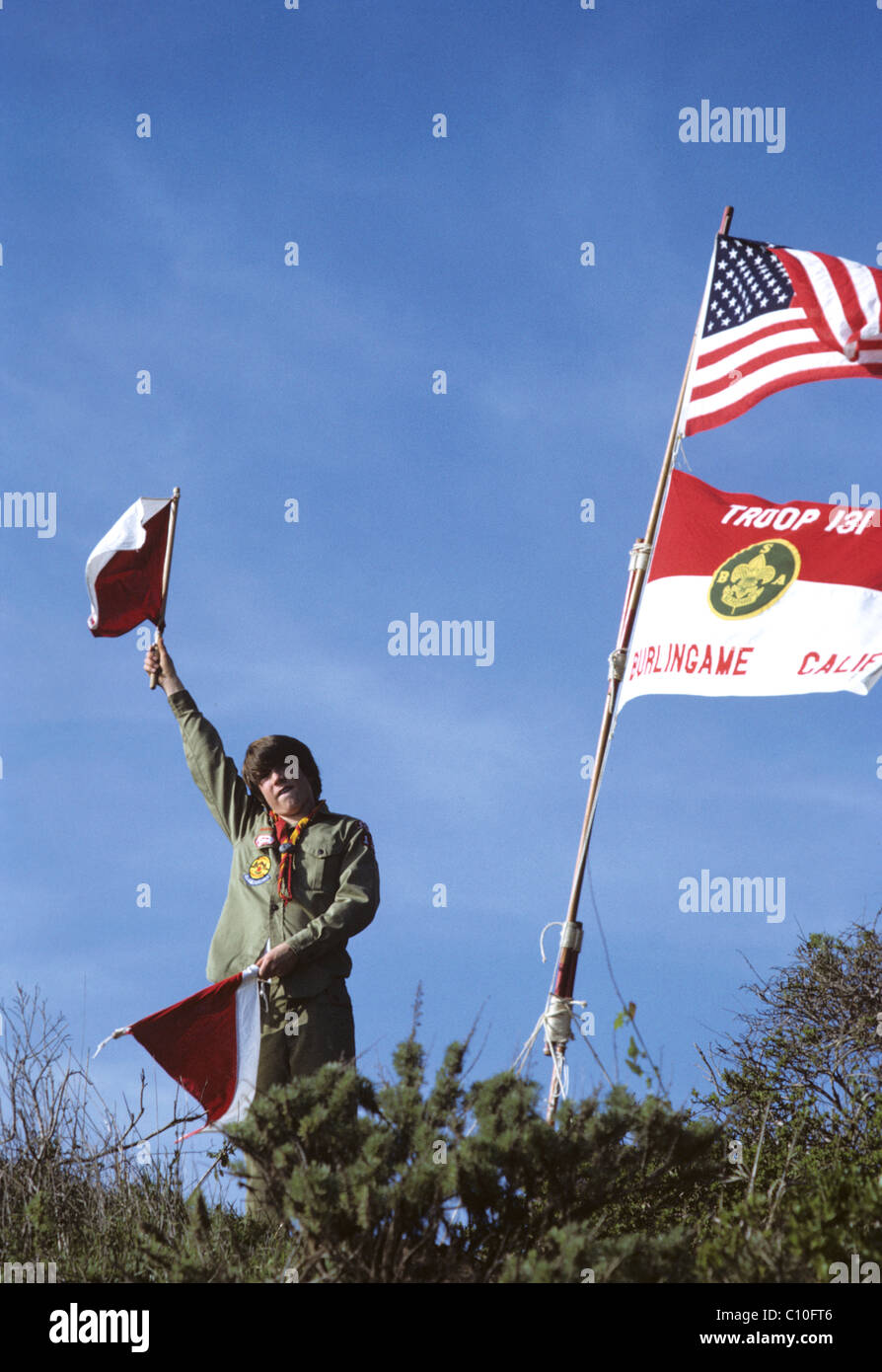 young Boy scout in uniform sends signals under  troop and United States flag Stock Photo