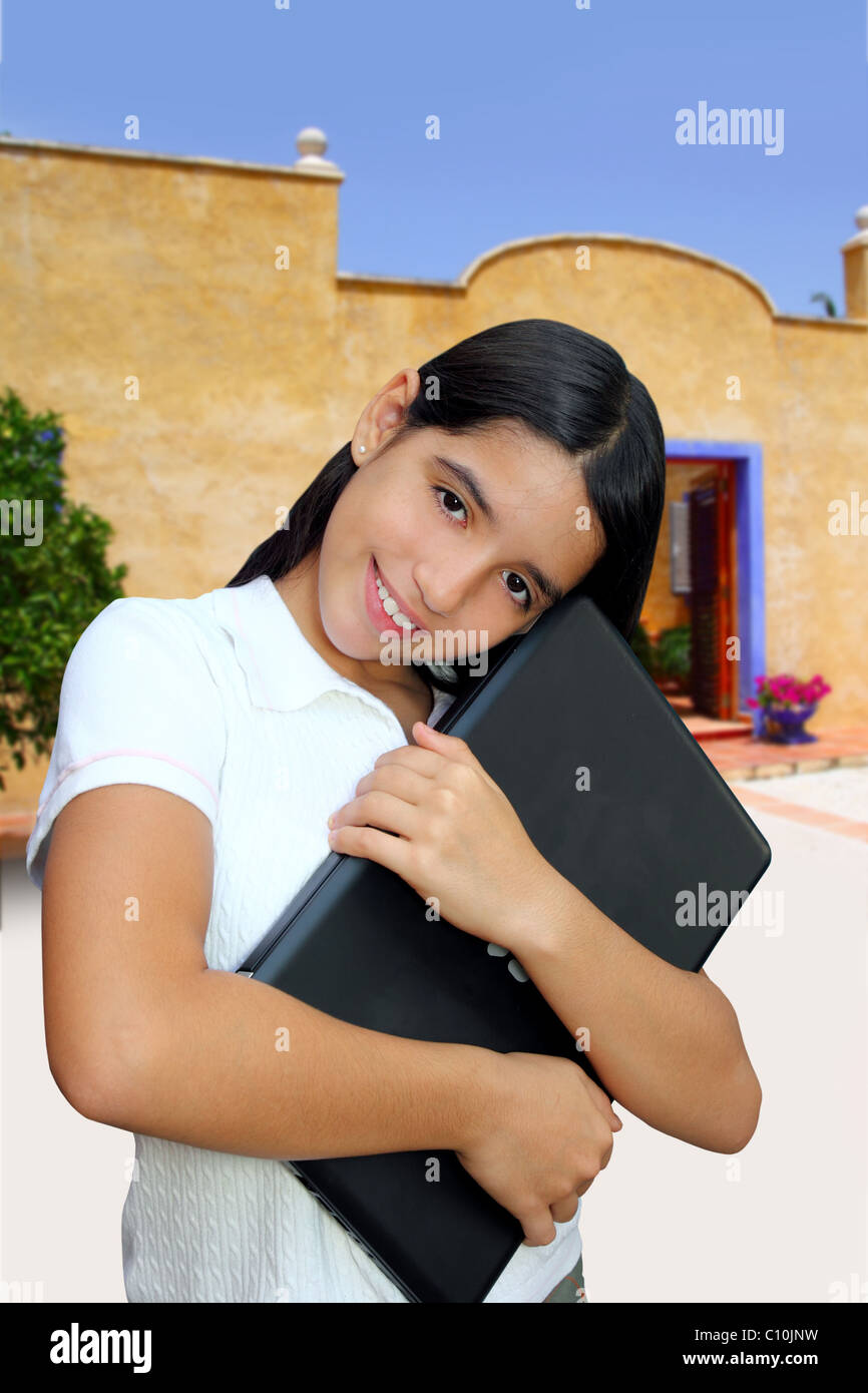 latin teenager brunette student hug laptop traditional yellow house Stock Photo