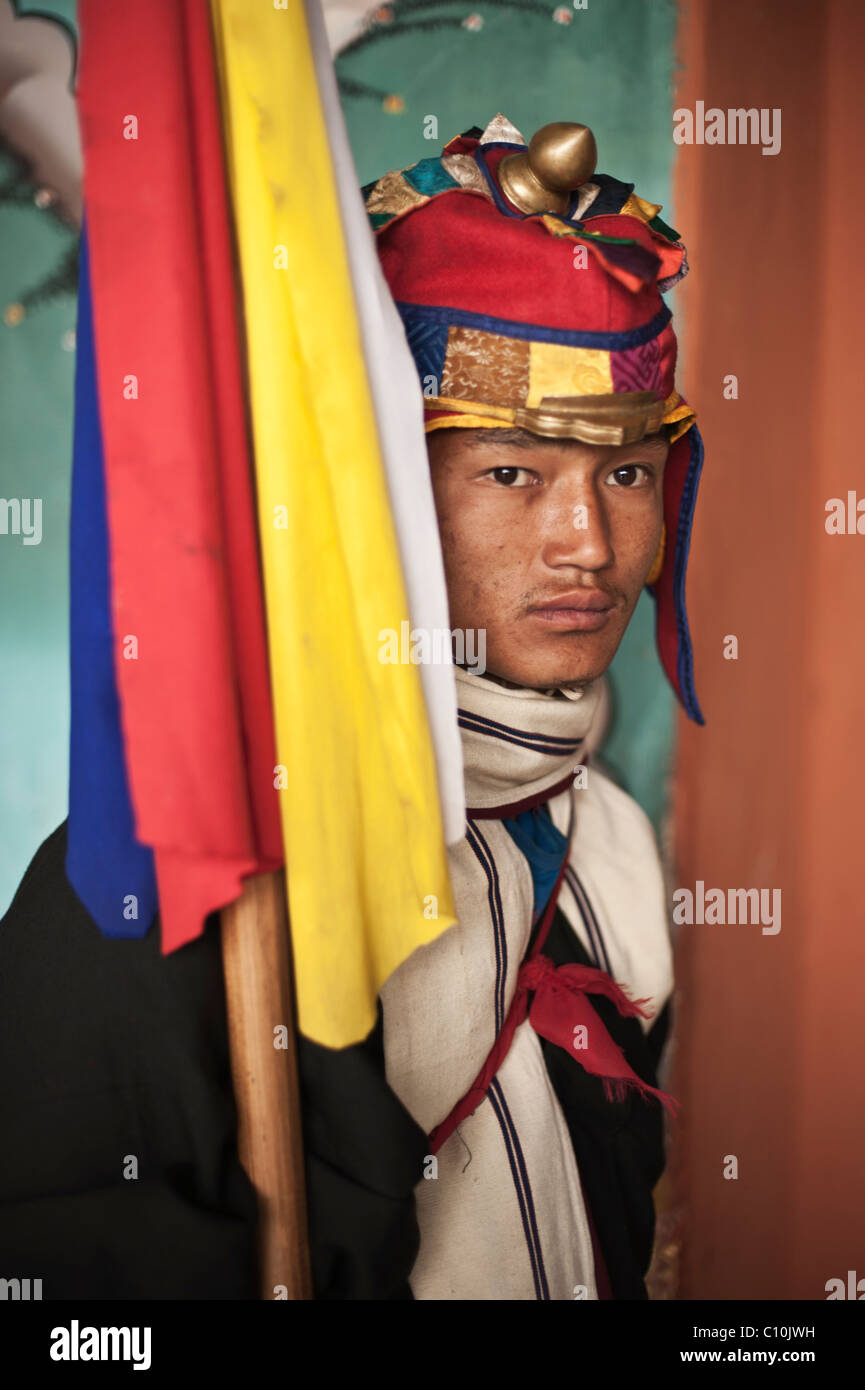 Bhutanese man dressed in colorful garb guards the entrance to the Punakha dzong during a major festival and holds a banner. Stock Photo