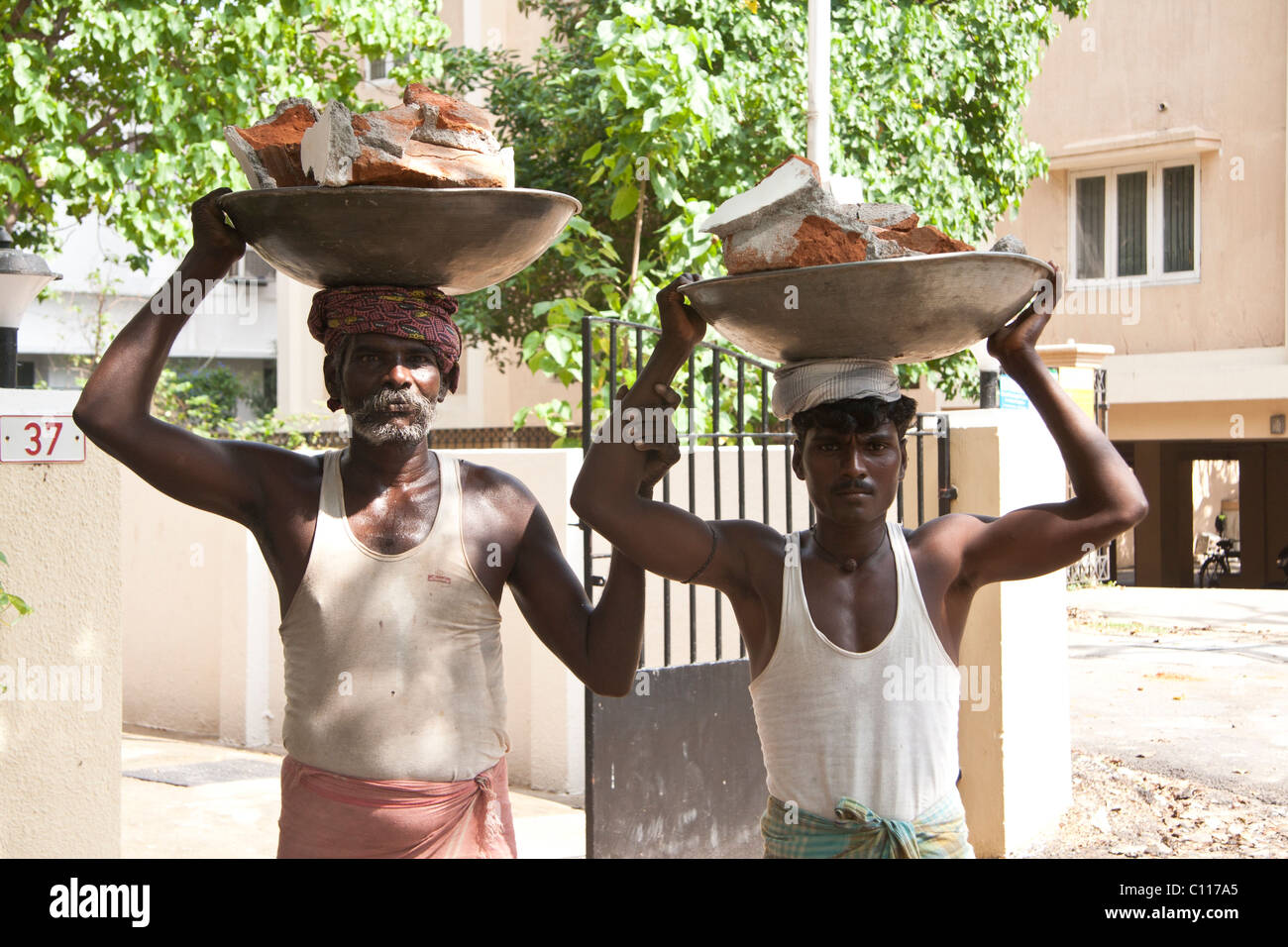 Two Indian builders carrying bricks on their heads Stock Photo