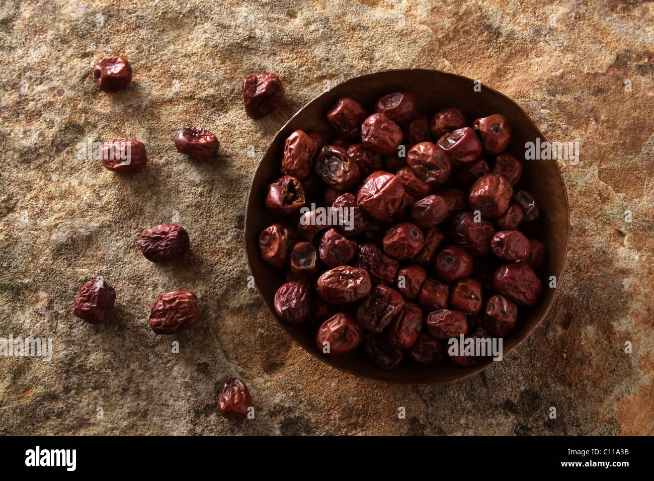 Jujube berries (Ziziphus jujuba) in a copper bowl on a stone surface Stock Photo