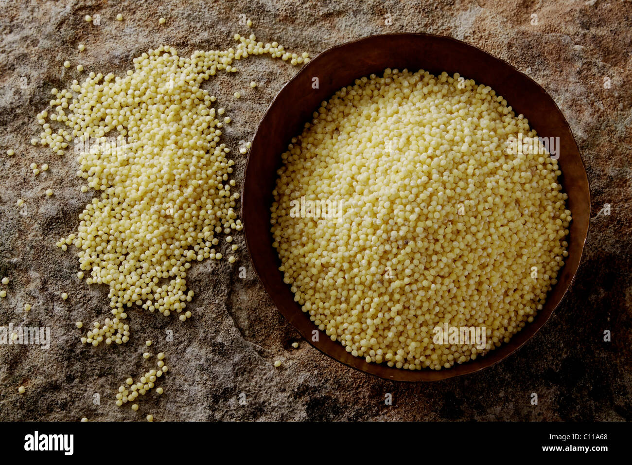 Millet (Panicum miliaceum) in a copper bowl on a stone surface Stock Photo