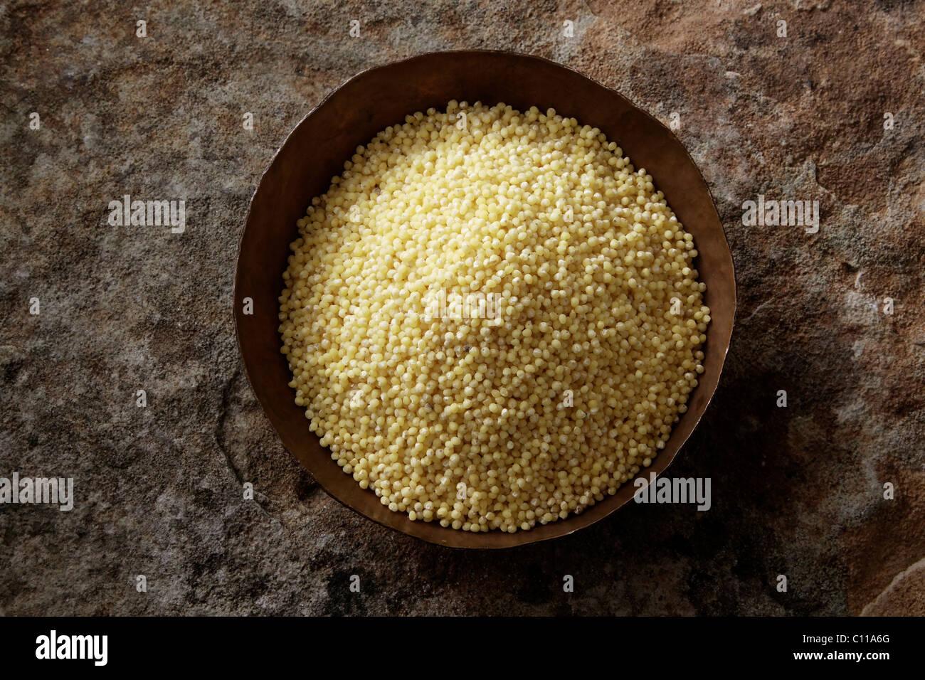 Millet (Panicum miliaceum) in a copper bowl on a stone surface Stock Photo