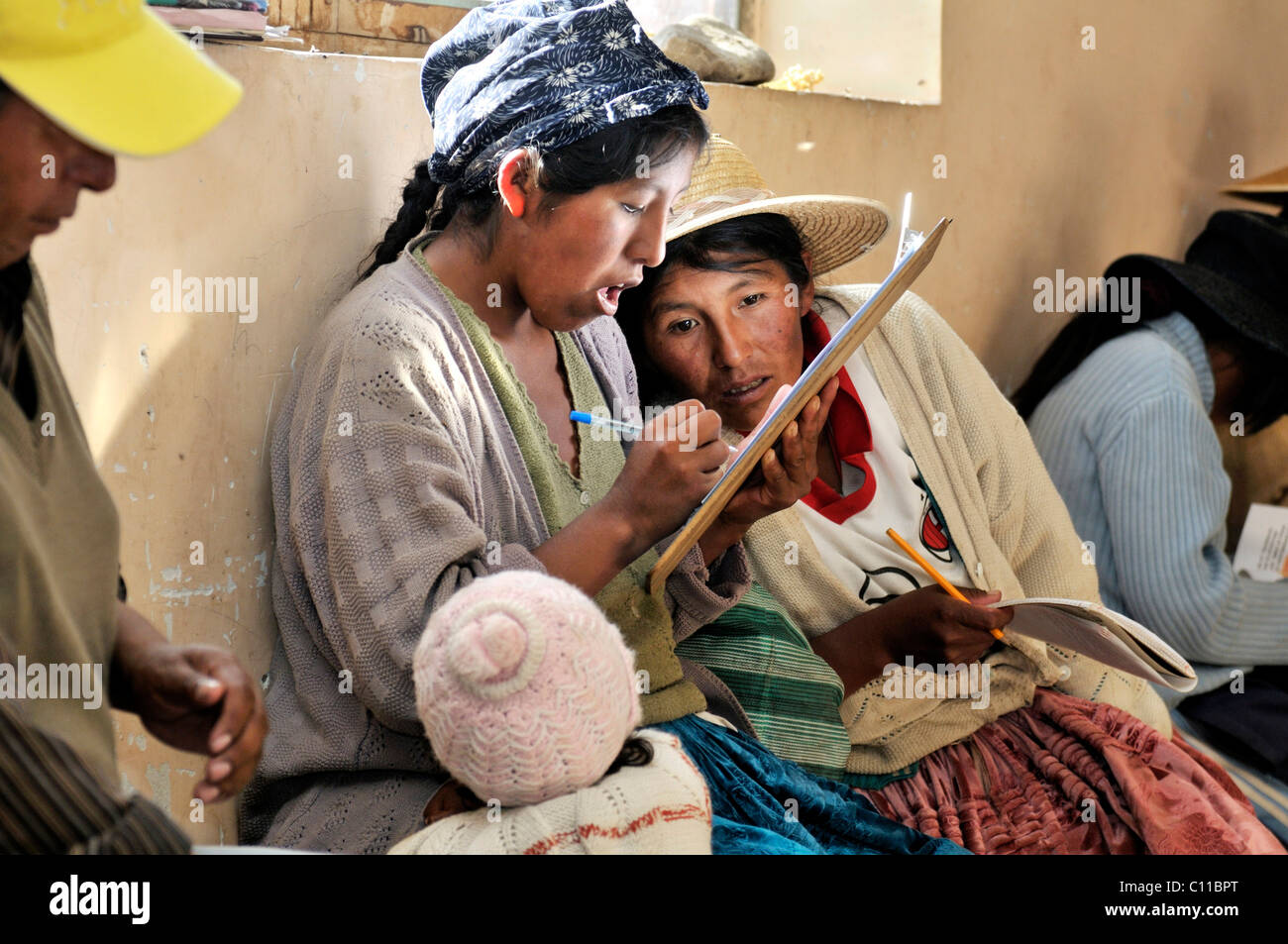 Women in traditional dress of the Quechua signing up for a course in the attendance list, Bolivian Altiplano highlands Stock Photo