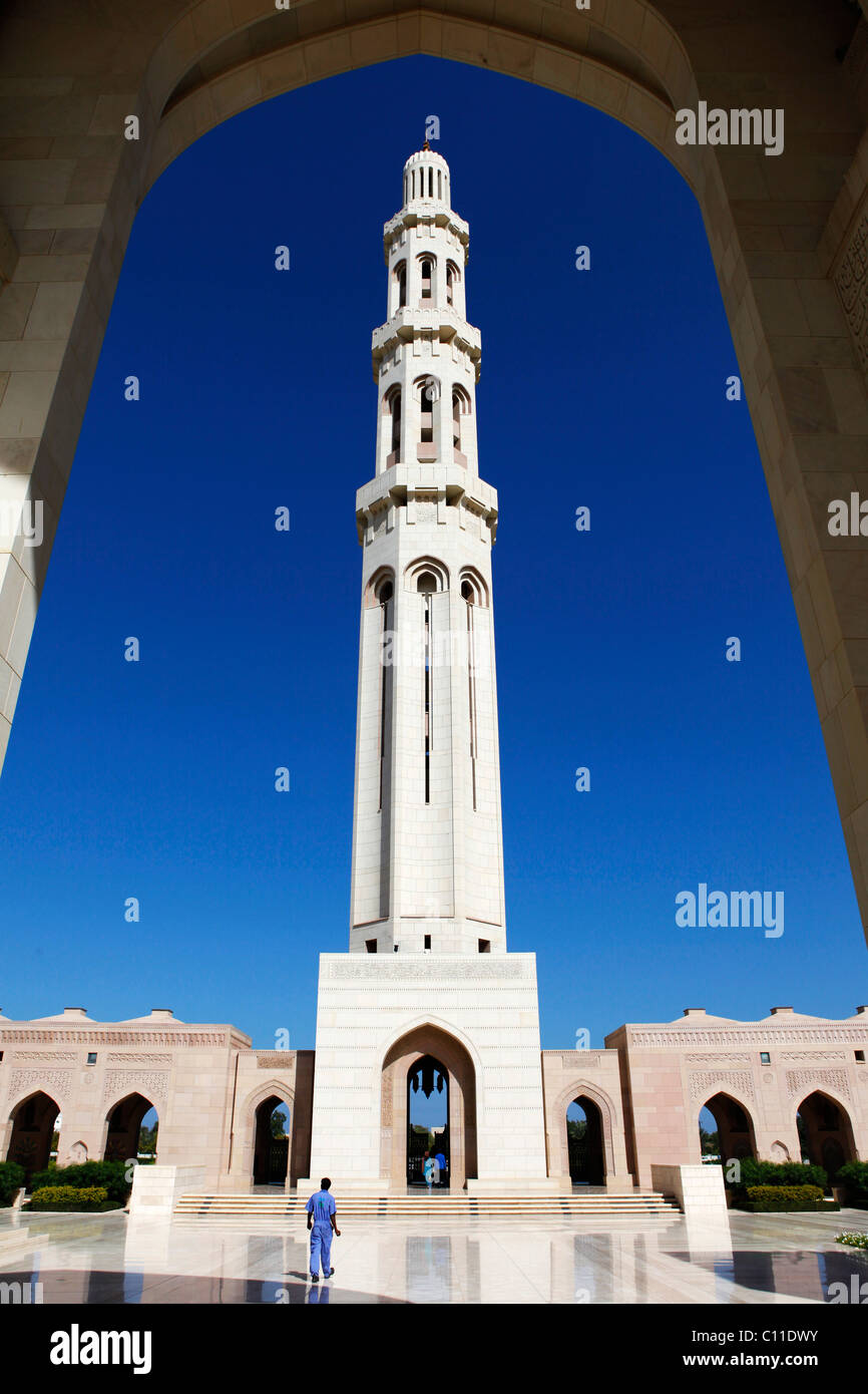 A worker in blue walks towards the minaret of the Sultan Qaboos Grand Mosque in Muscat, Oman. Stock Photo