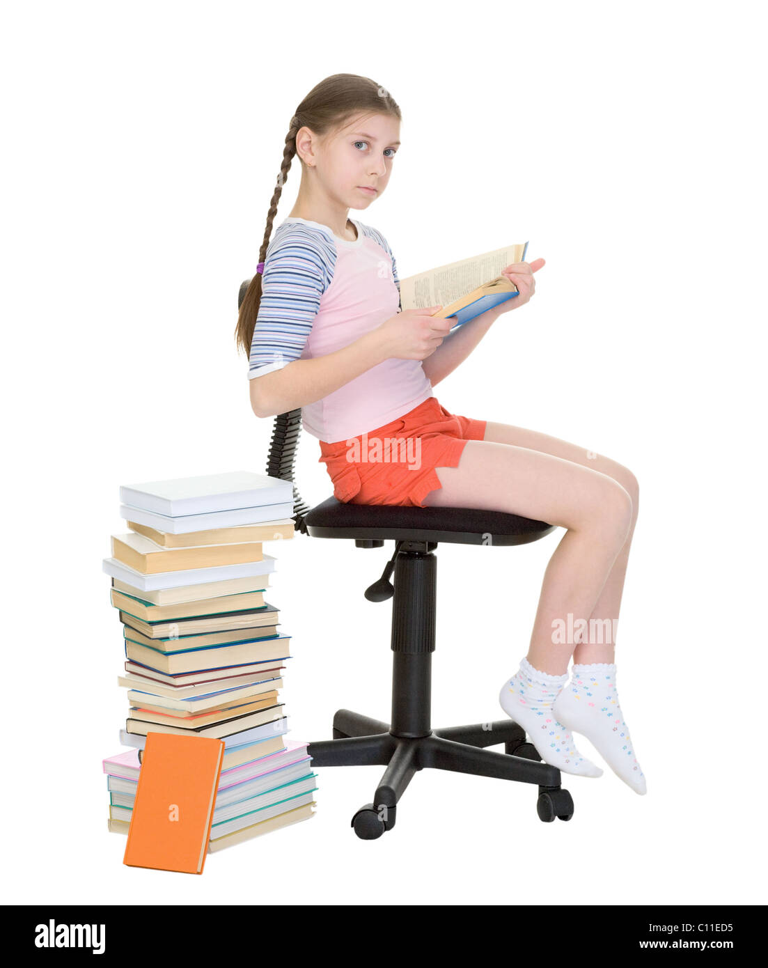 Schoolgirl learns lessons near big pile of textbooks Stock Photo