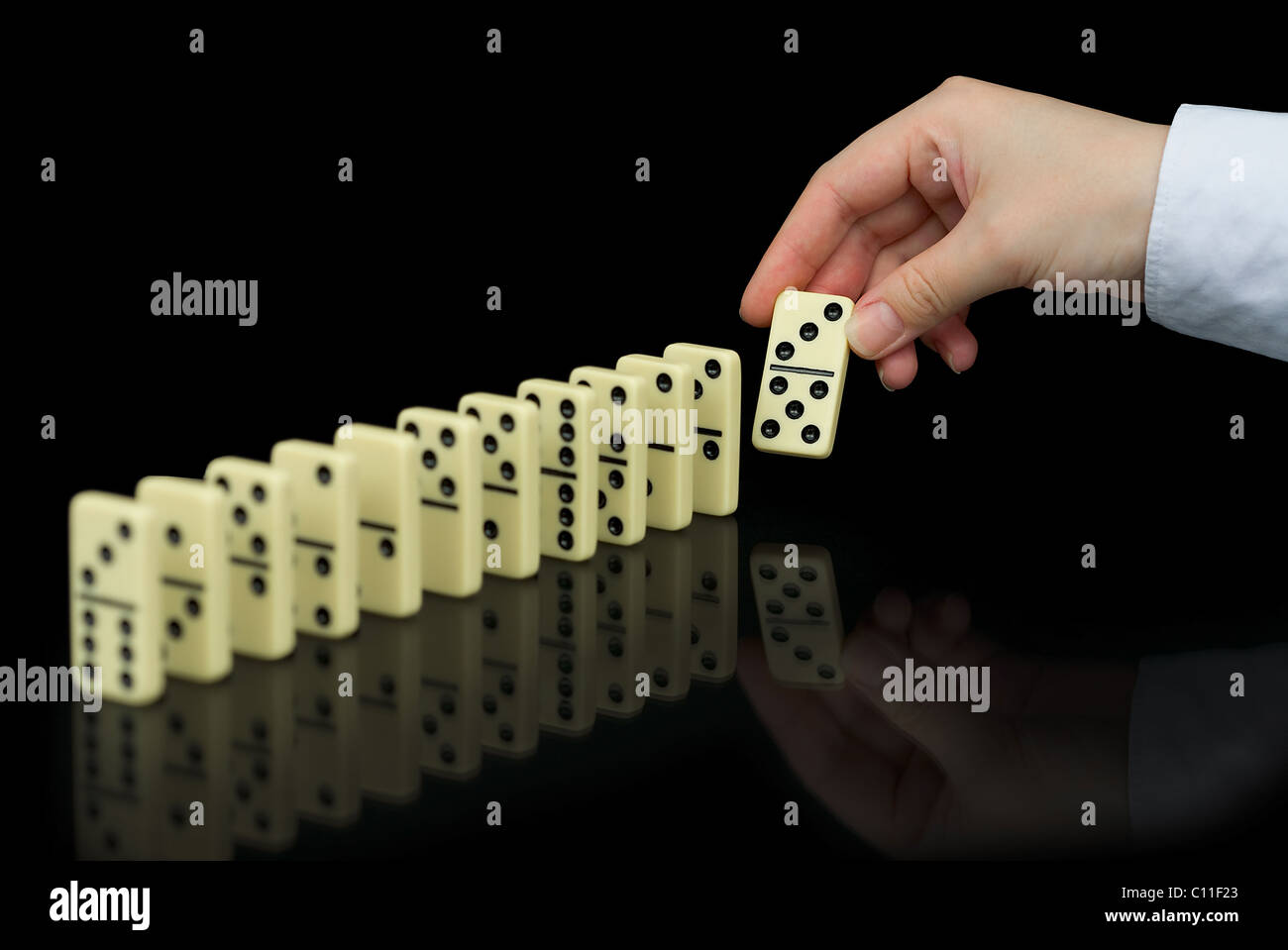 Hand builds a line of dominoes on black background Stock Photo