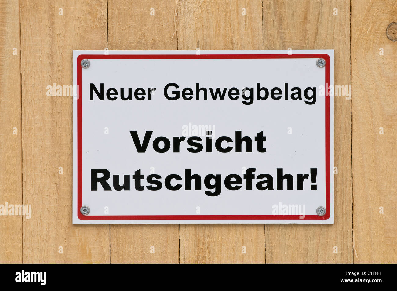 Sign on wooden board fence, Neuer Gehwegbelag Vorsicht Rutschgefahr, new walkway surface, caution slip hazard! Stock Photo