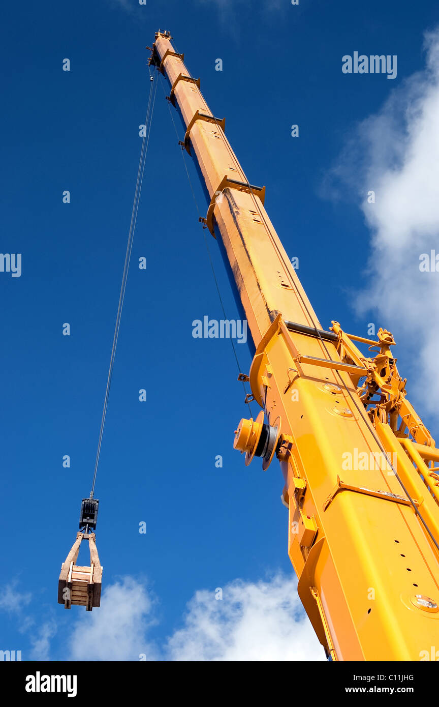 Yellow mobile crane hydraulic boom raises cargo against a blue sky