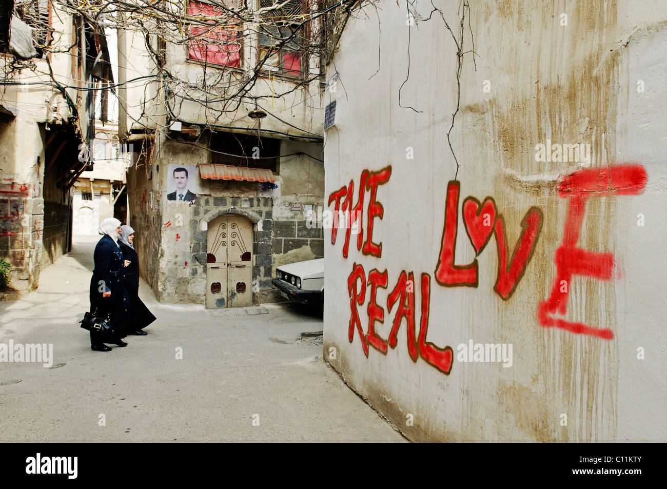 Women with headscarves and graffiti, 'Real Love', in the historic centre of Damascus, photo of Bashar Al Assad in the back Stock Photo
