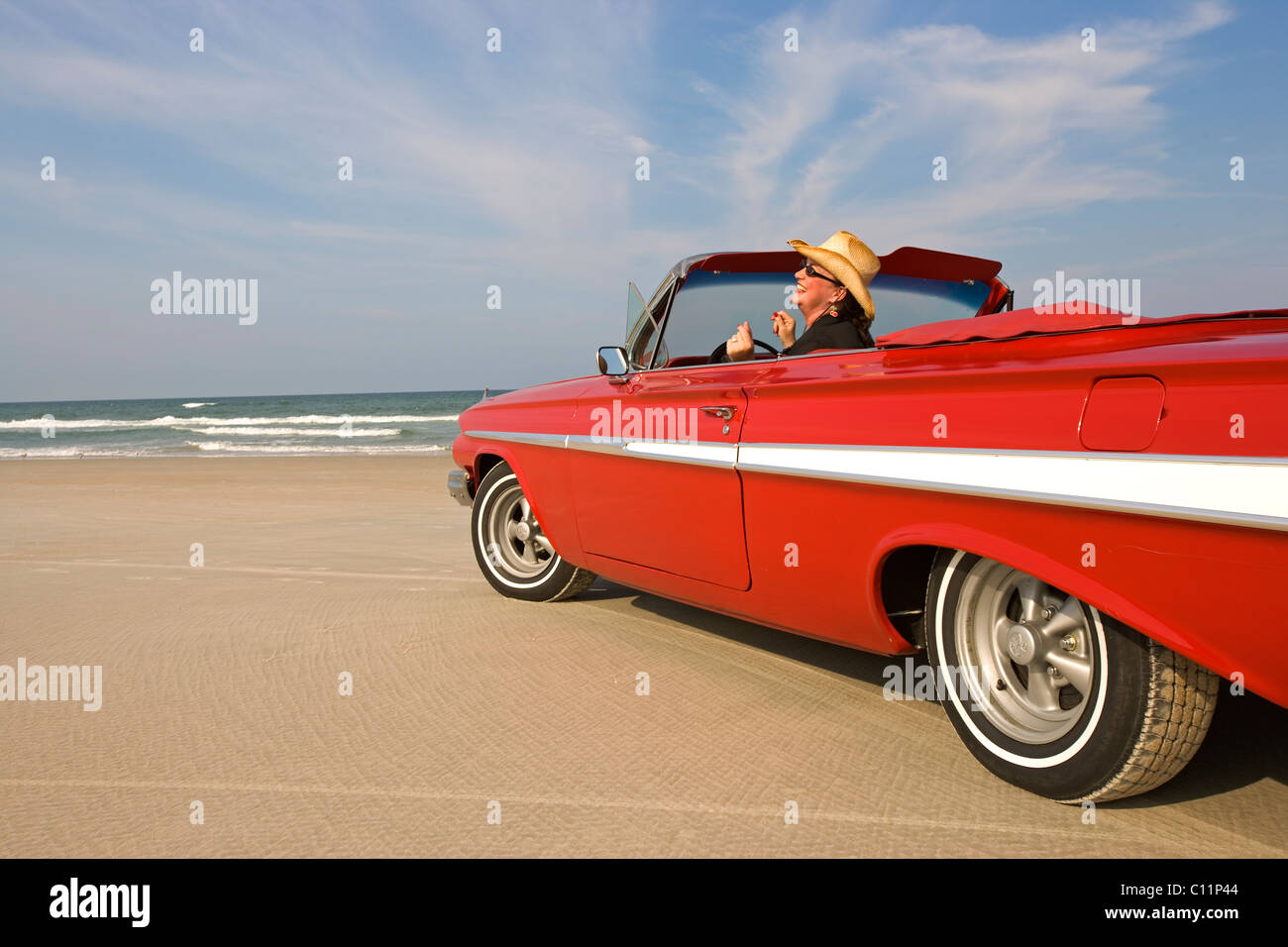 Woman sitting in classic red convertible car on the beach in Daytona Beach, Florida  snapping fingers in glee Stock Photo