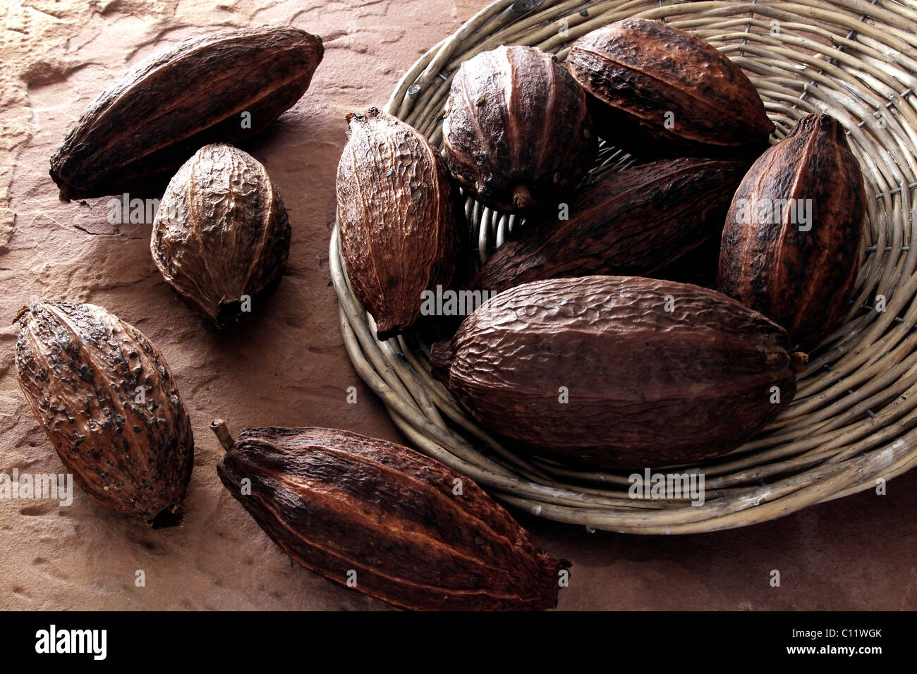 Cocoa beans, tipped from a wicker plate on sandstone Stock Photo