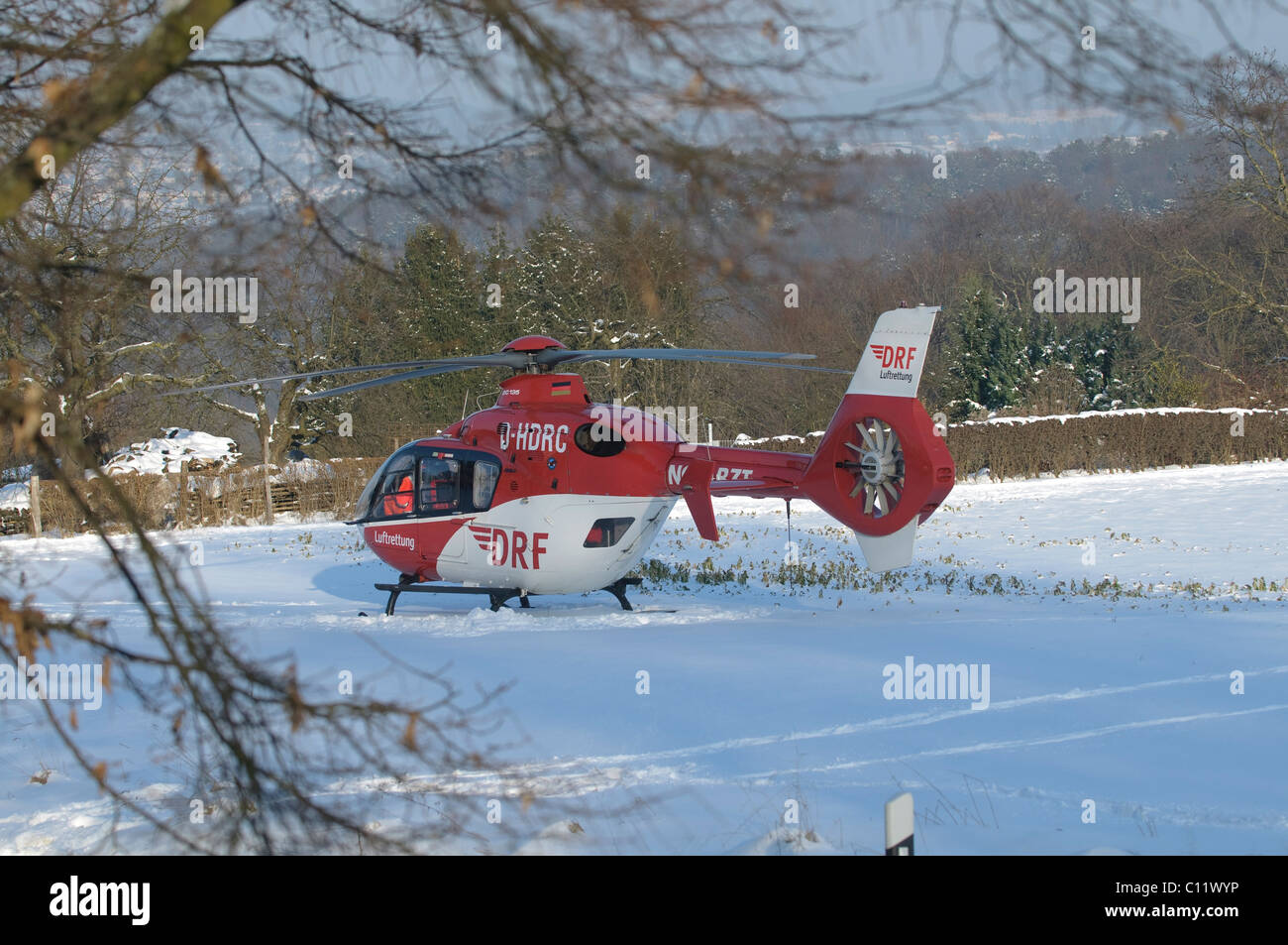 Rescue helicopter Christoph 41, identifier D-HDRC, landing on a snow-covered meadow, in front a Porsche Cayenne ambulance of the Stock Photo