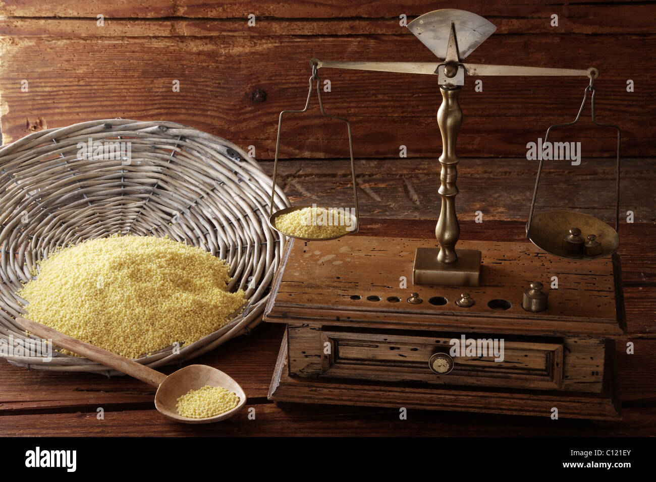 Antique scales weighing grains of Millet (Panicum miliaceum) on a wooden surface Stock Photo
