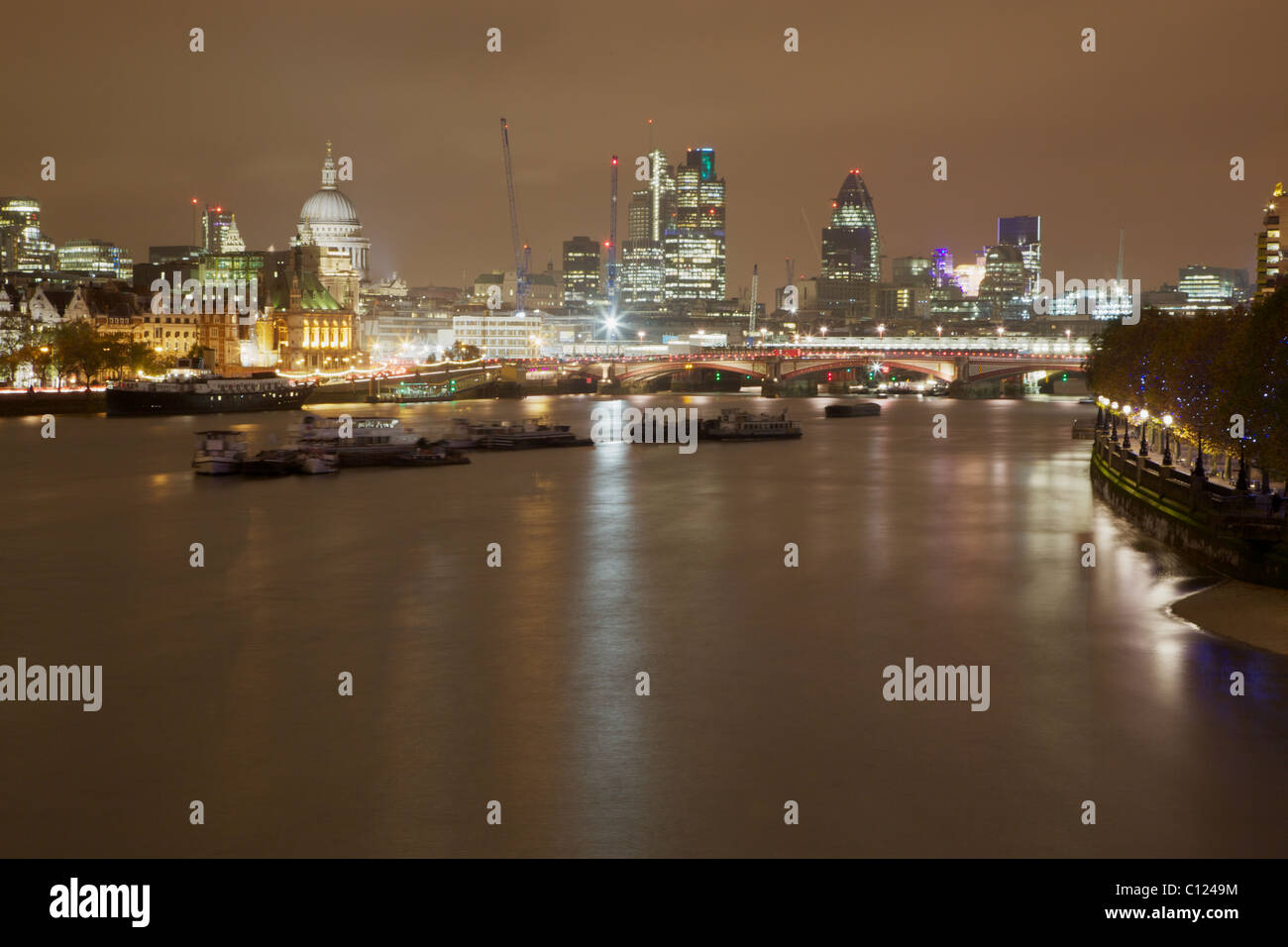 A night view of the City Of London skyline and River Thames. A long exposure gives the water a flat calm appearance. Stock Photo