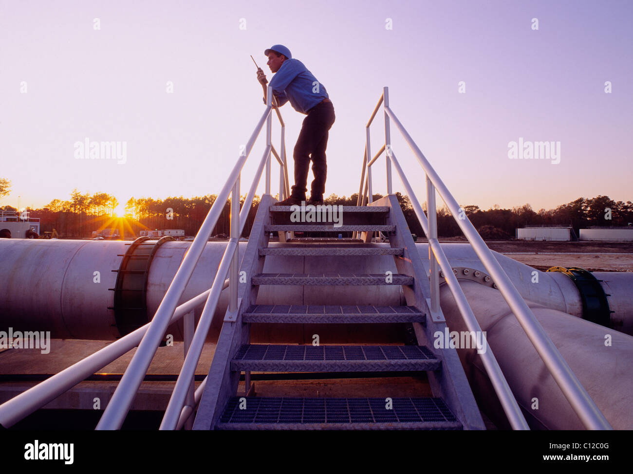 Engineer on a walkie talkie radio at sunset at a waste water treatment plant, Houston, Texas, USA Stock Photo