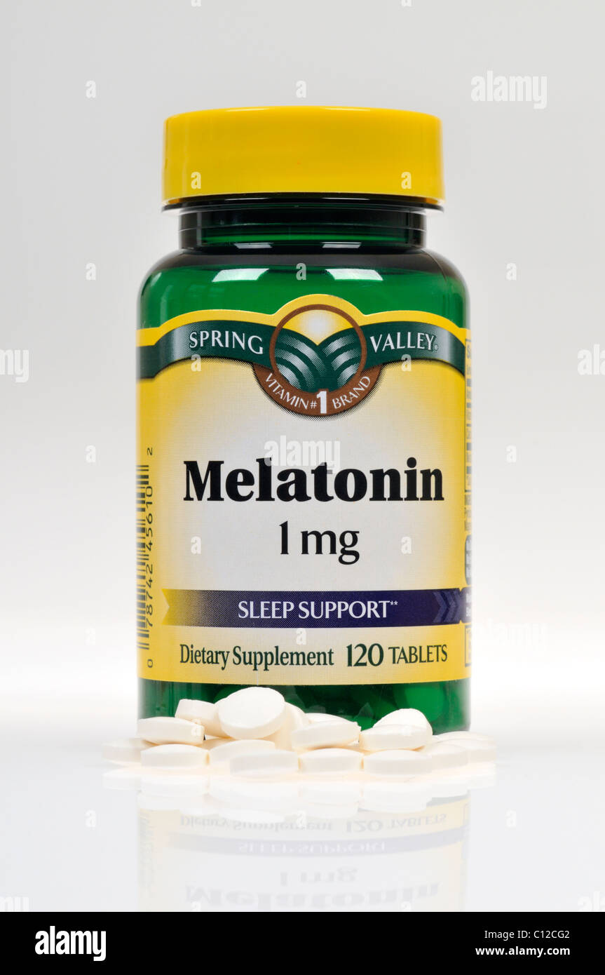 Bottle of Spring Valley Melatonin dietary supplement with tablets scattered on white background, cutout. Stock Photo