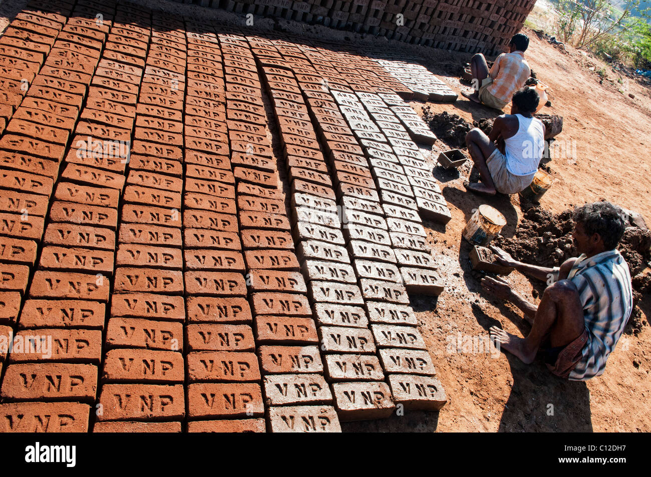 Indian men making house bricks by hand using a mould and wet clay / mud. Drying them in the sun before firing them hard. Andhra Pradesh, India Stock Photo