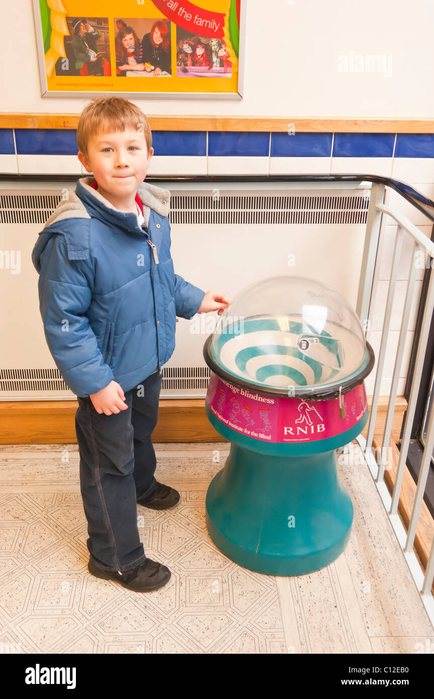 A MODEL RELEASED six year old boy puts money in a charity box for the Royal national Institute for the Blind in the Uk Stock Photo