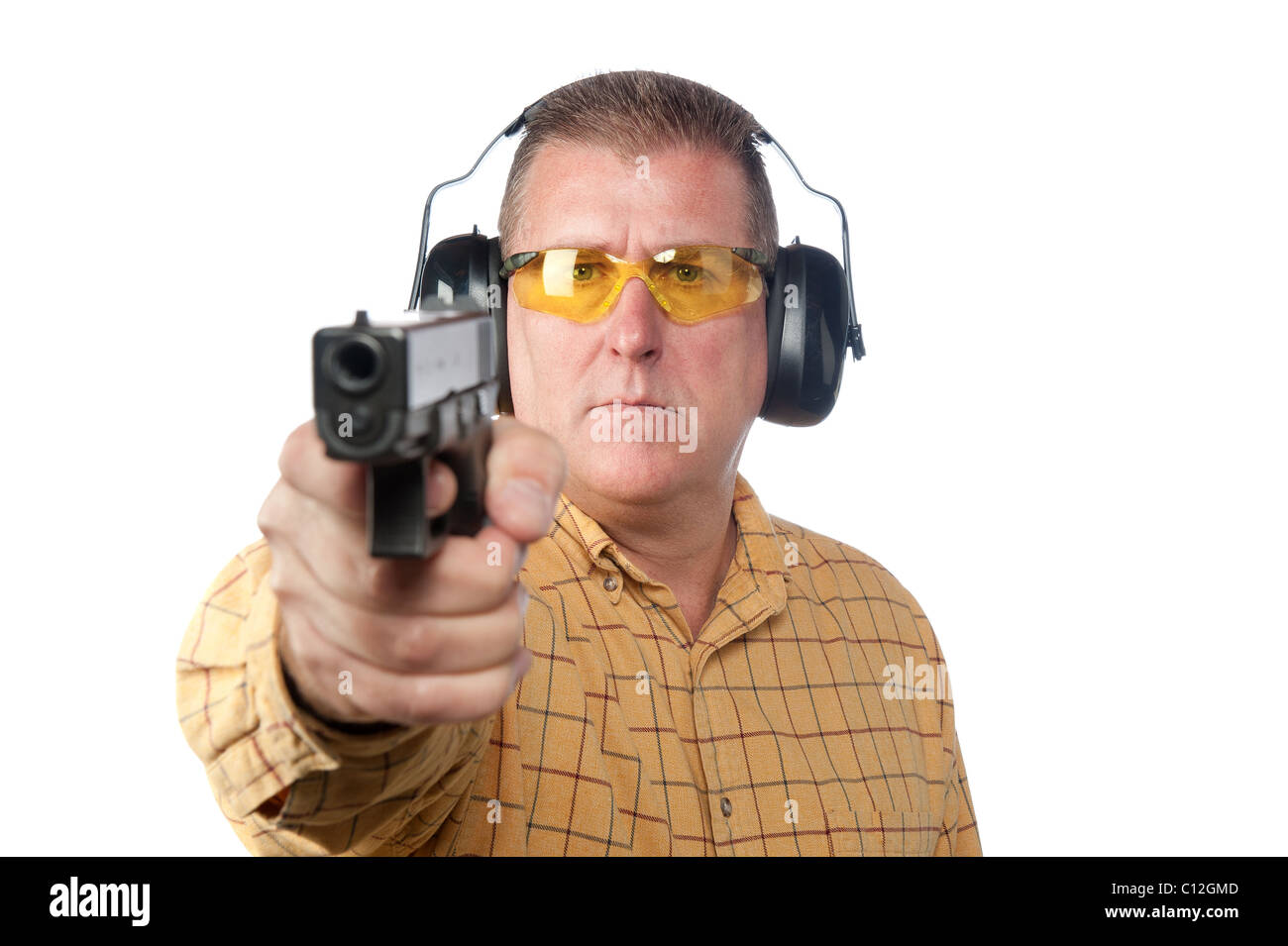 A man aims a handgun while wearing proper safety equipment such as safety glasses and hearing protection. Stock Photo